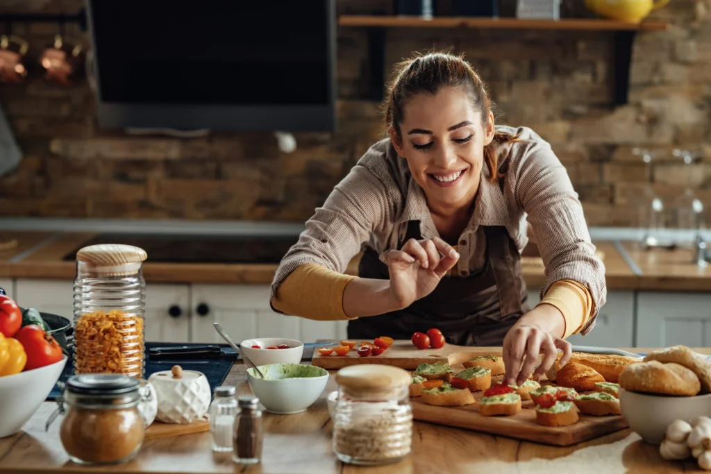 young smiling woman making bruschetta with healthy ingredients while preparing food kitchen